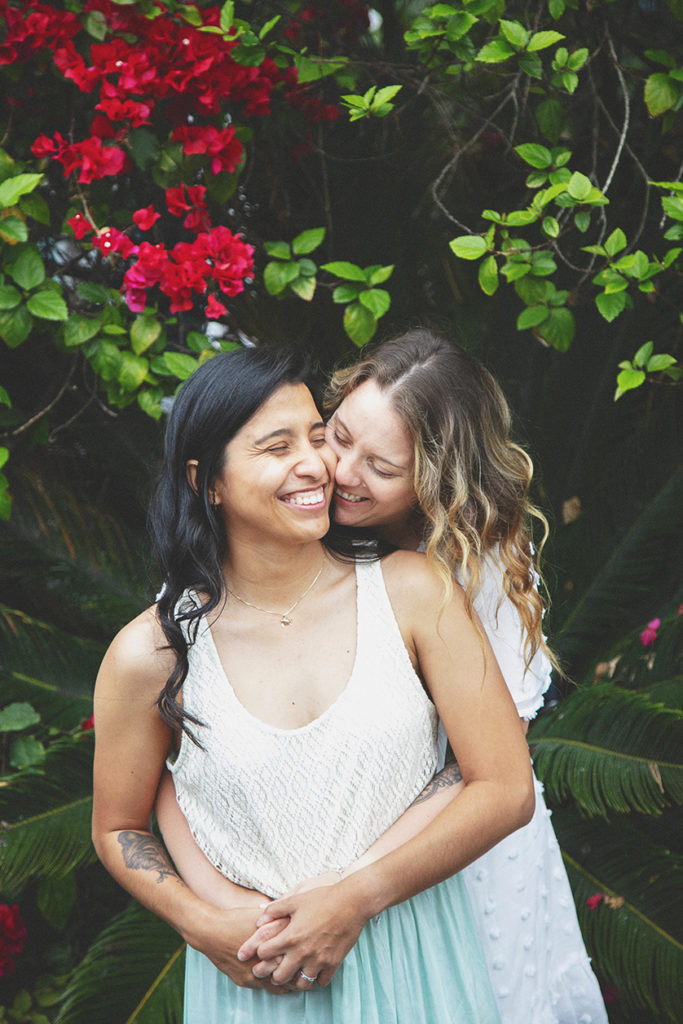 The two brides share a sweet moment together in front of a beautiful green bougainvillea vine