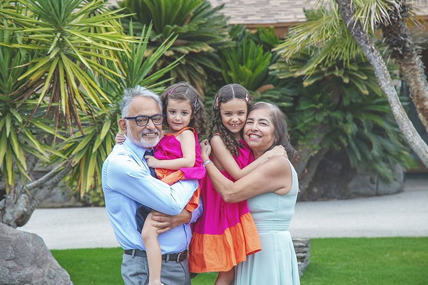 Grandma and Grandpa squeeze their grandaughters in front of a garden setting