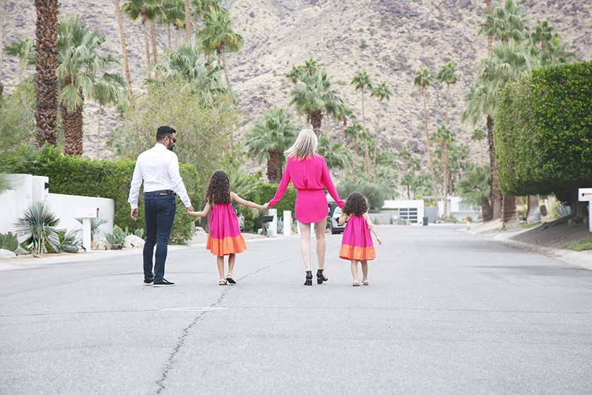 Mom and dad and two young girls stroll hand in hand, magenta pink dresses.