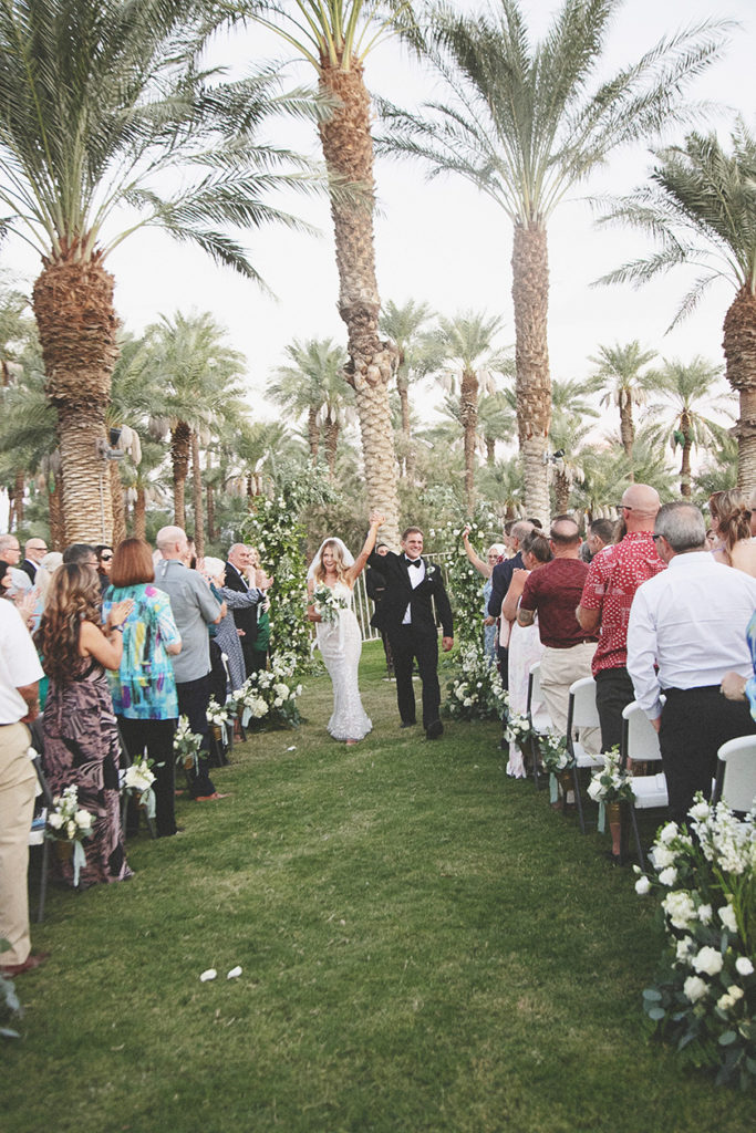 Bride and groom walk happily down the aisle, arms held high in celebration