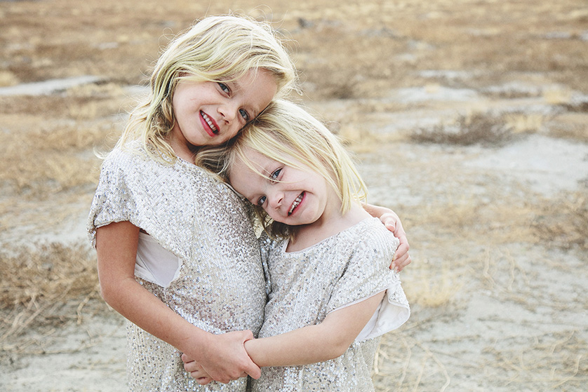 Young sisters in sequined outfits embrace sweetly and smile for the camera