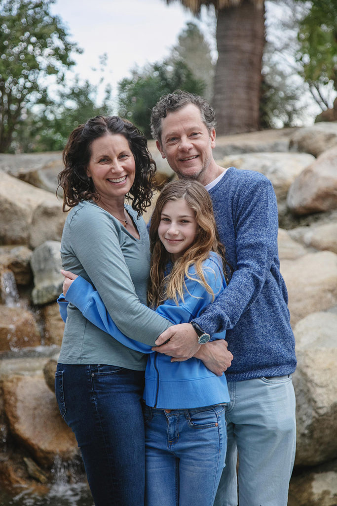 Family of three hug tight for a family photo in front of the waterfall