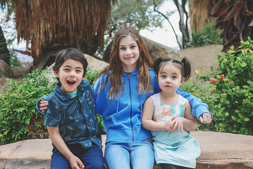 Three cousins sit on a stone bench for a camera aware portrait