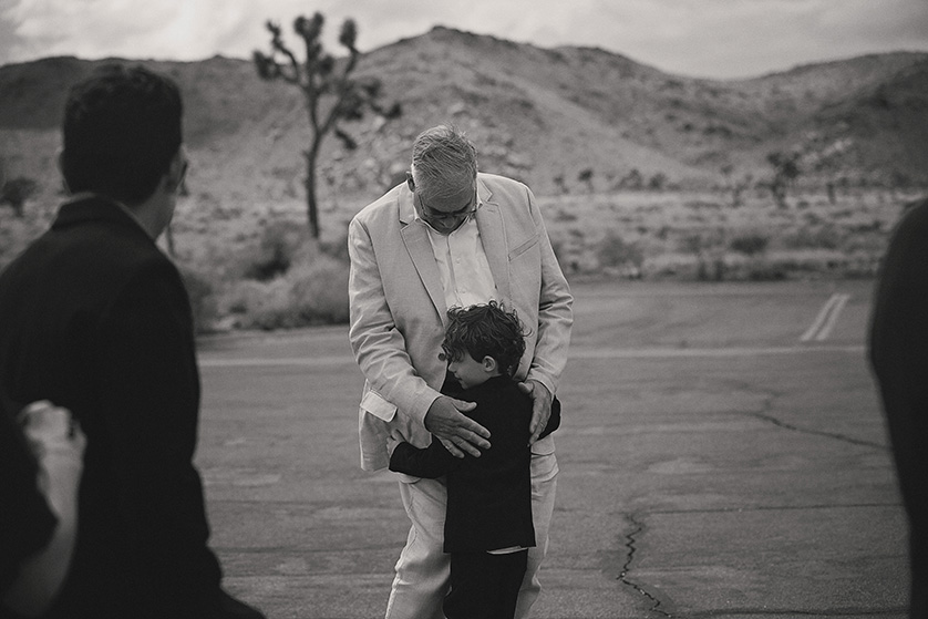 Black and white candid photo of the ring bearer hugging his grandfather