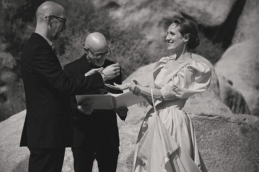 A bride and groom getting married on a windy day at the base of large rocks in Joshua Tree park.