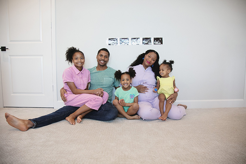 Family of five seated on the floor with ultrasound photos above them, to announce the new baby on the way.