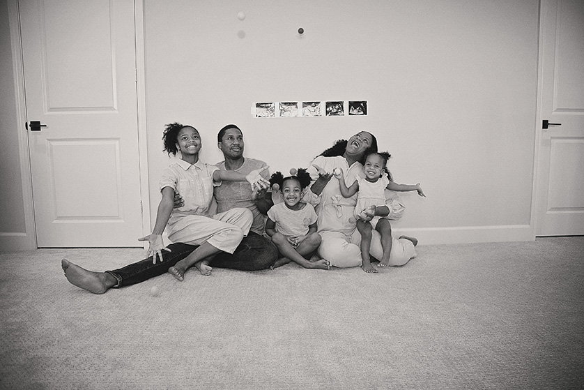 A fun black and white photo of a growing family having fun, throwing plastic balls in the air.