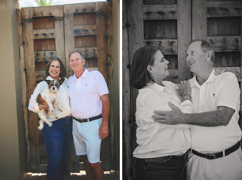 Grandparents pose with big smiles in front of wooden doors in La Quinta home