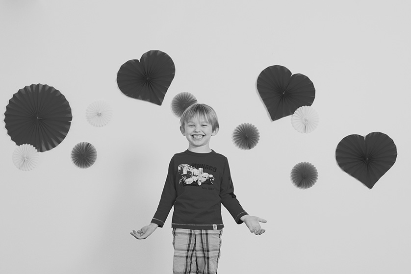 Smiling boy in plaid shorts against a backdrop of hearts and decorations.