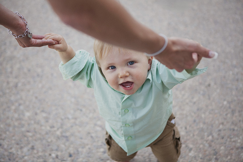 Toddler in green shirt holding hands, smiling up at the camera