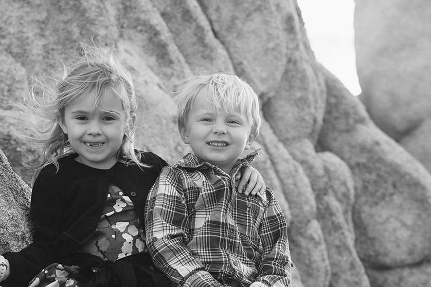 Black-and-white photo of two smiling children sitting on rocks.