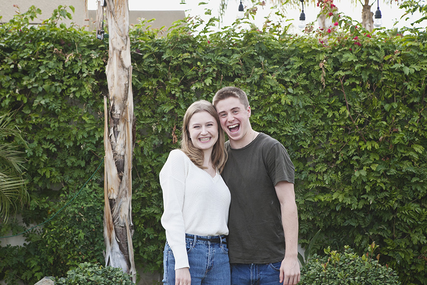 Smiling young couple posing in a lush green outdoor setting.