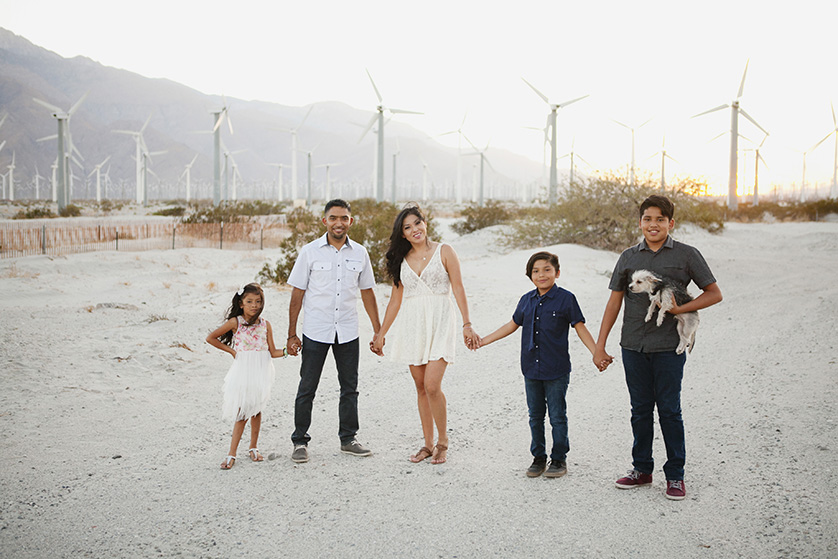 Family holding hands outdoors with wind turbines in the background.