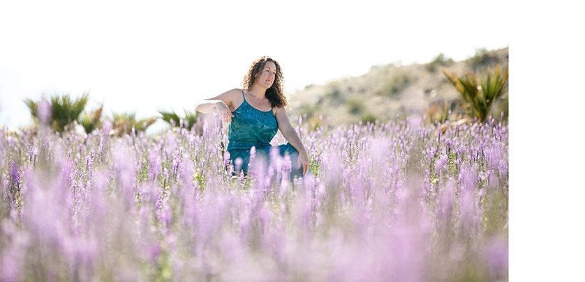 Woman with curly hair sits in a field of wildflowers