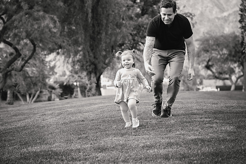 Candid photo of dad chasing toddler in the park