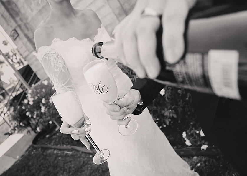 Black and white photo detail of groom pouring champagne into a glass