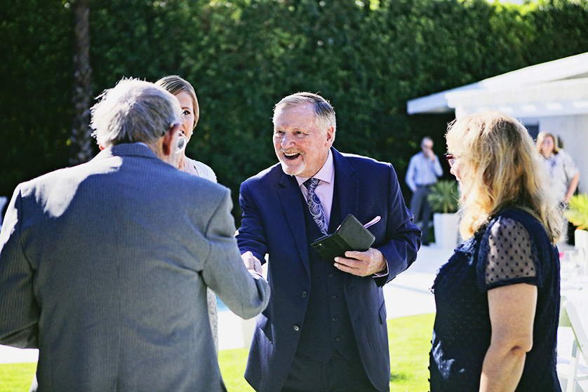 Officiant warmly greets wedding guests in a sunny Palm Springs backyard.
