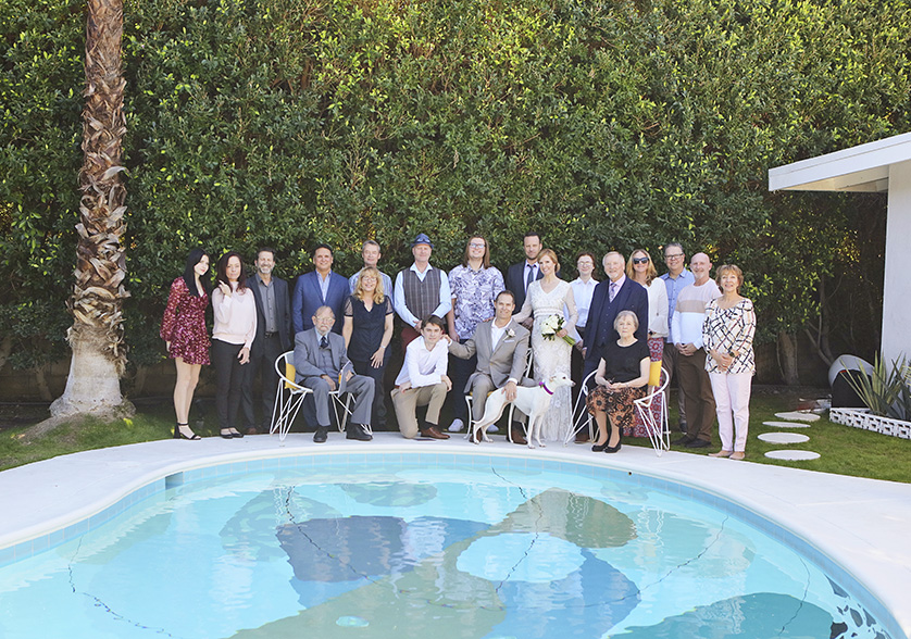 Bride and groom pose with family and friends beside a vintage-style pool during their Palm Springs backyard wedding.