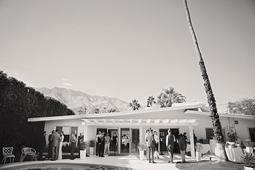 Guests mingle outside a mid-century modern Palm Springs home during a stylish backyard wedding celebration.