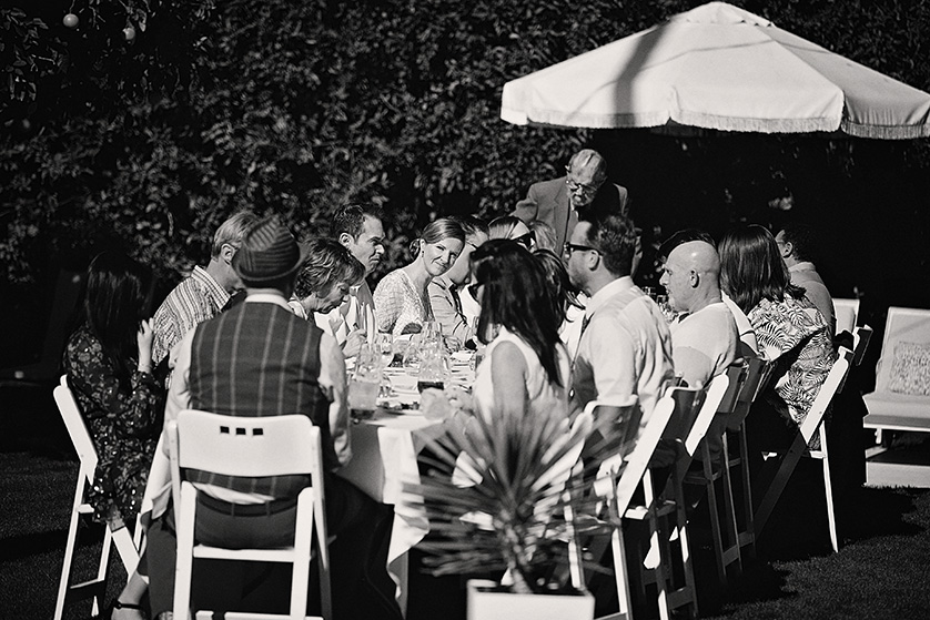 Black-and-white photo of wedding guests gathered at a long outdoor table during a backyard reception in Palm Springs.