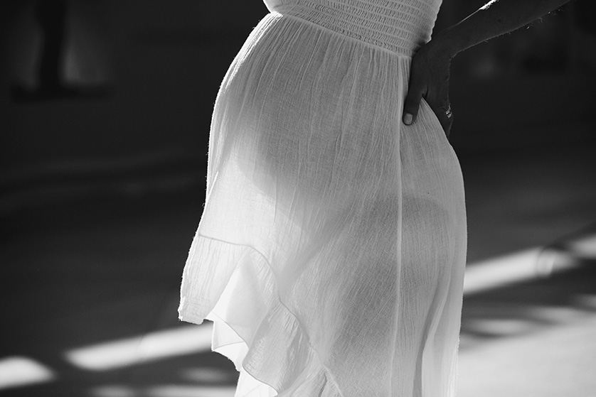 Pregnant woman in flowing white dress, lit by the sun