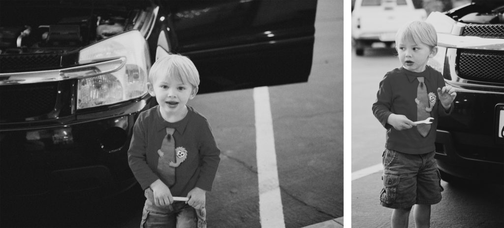 Young boy with a toy wrench playing near a car in a parking lot, dressed in a fun shirt with a cartoon tie.