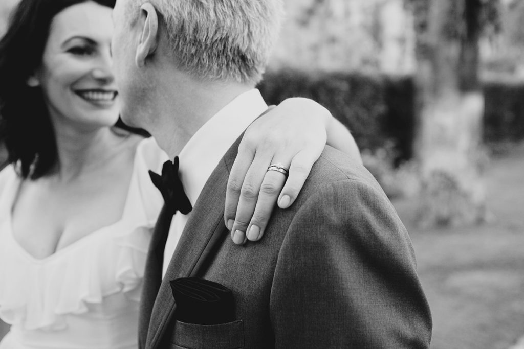 Bride and groom share a joyful moment, the bride’s hand resting on the groom’s shoulder with her wedding ring in focus.