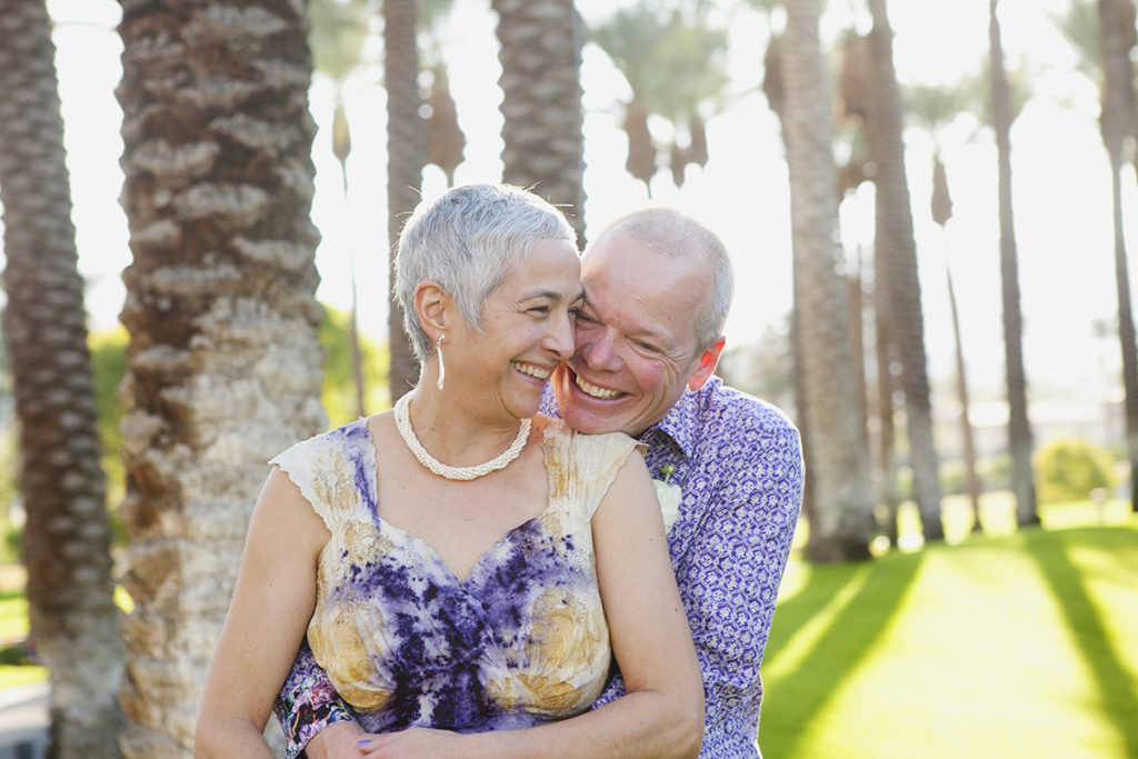 Couple share a joyful embrace among palm trees during their Palm Springs wedding.