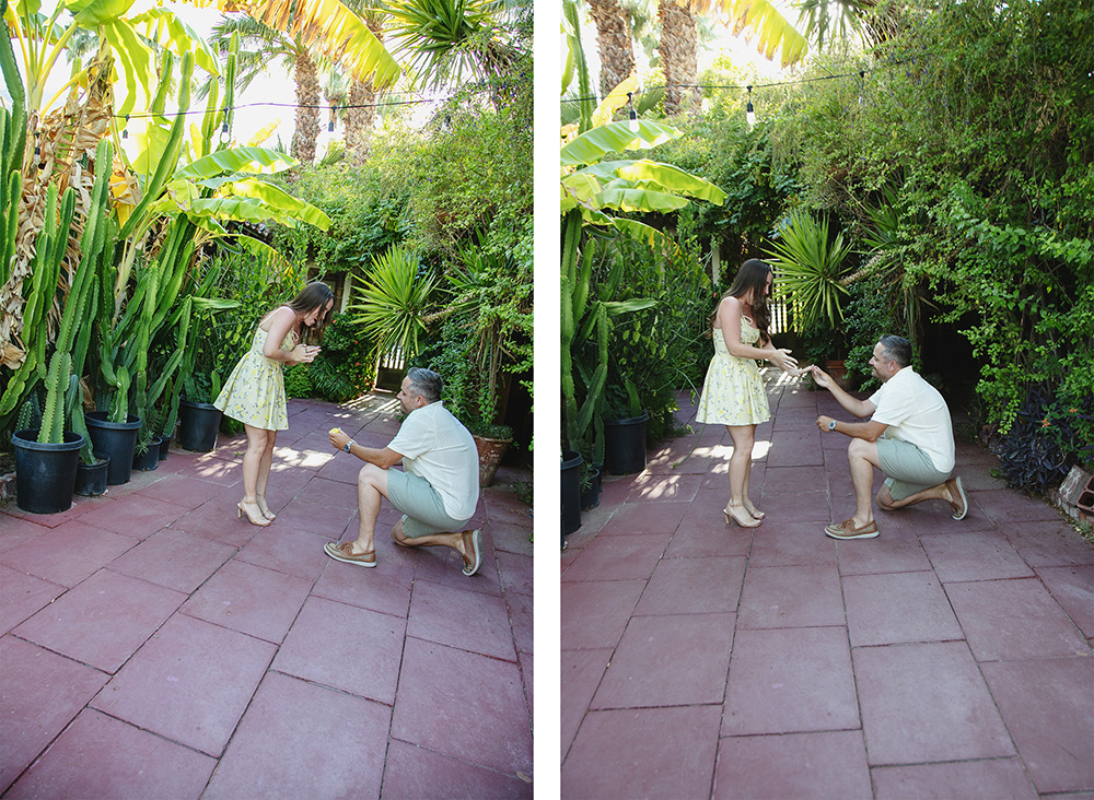 Man on one knee proposes at Casa Monte Vista in Palm Springs as his partner reacts with joyful surprise, reaching out with excitement among lush greenery.