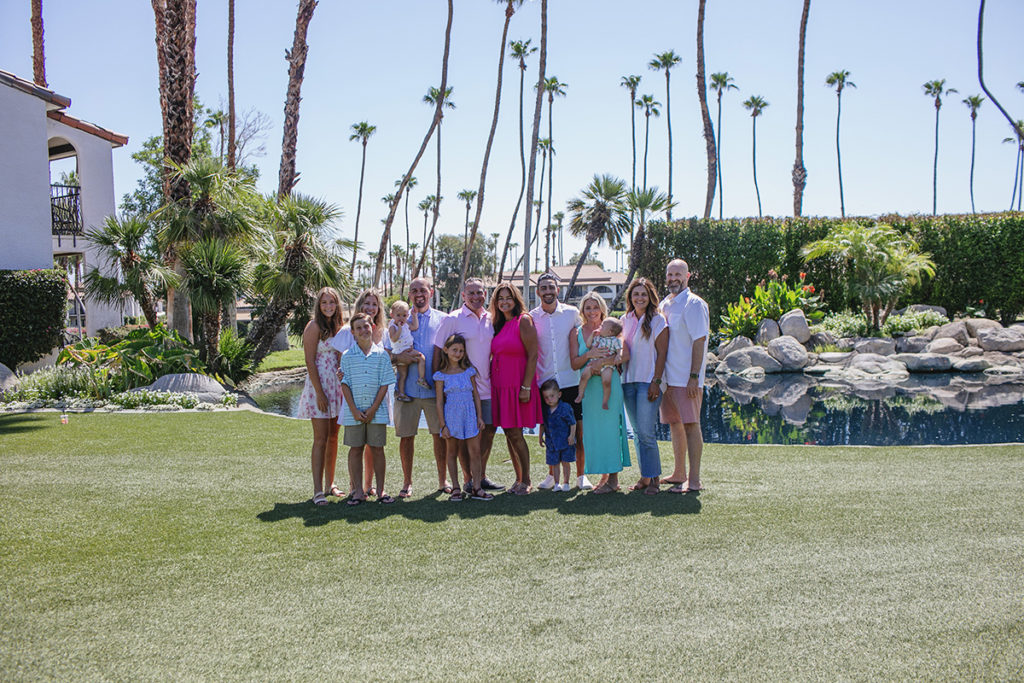 A large family poses together on a sunny lawn by a pond with palm trees in Palm Springs, California.