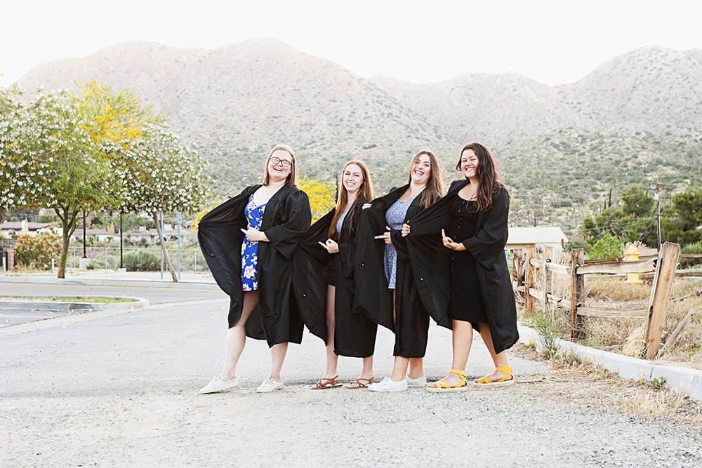 Best friends make a playful gesture behind their graduation robes
