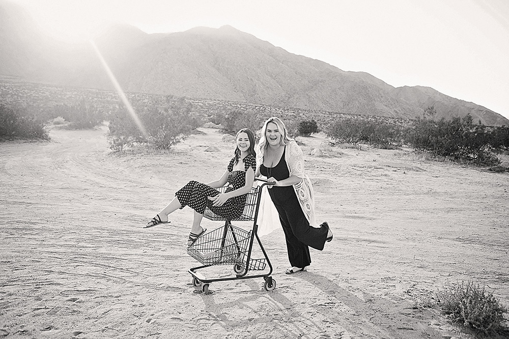 Two sisters graduating from high school pose playfully in a shopping cart