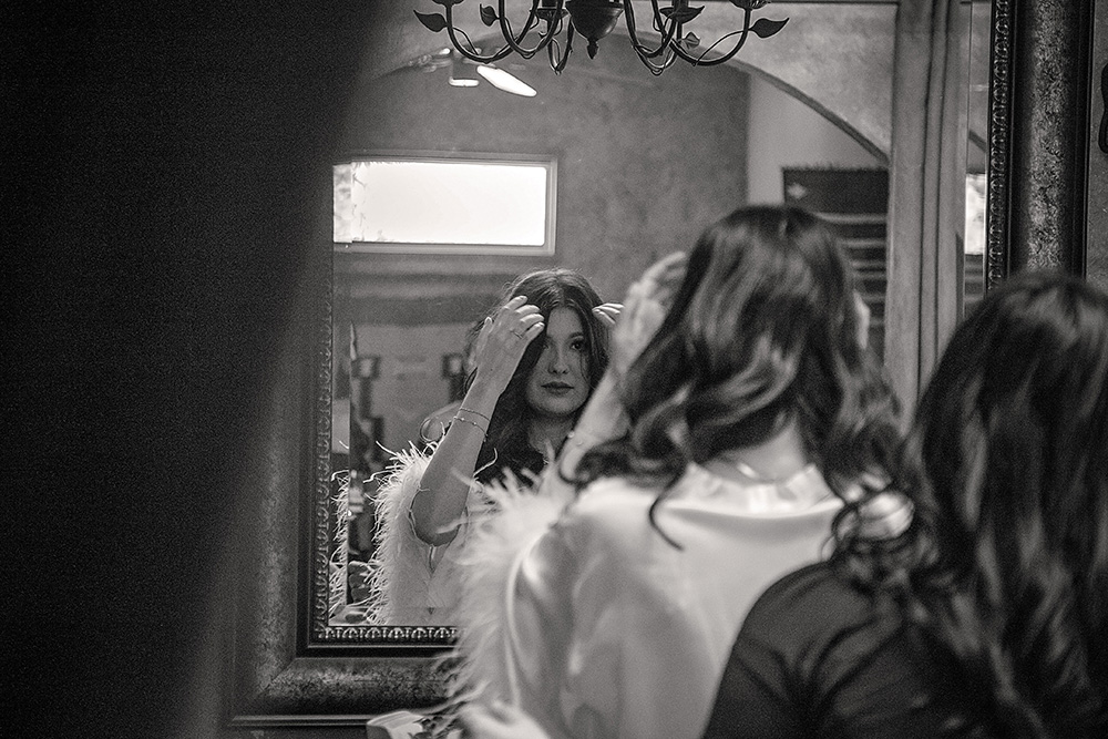 Bride adjusting her hair in a mirror while getting ready at Bubbling Wells Ranch, captured in black and white documentary wedding photography