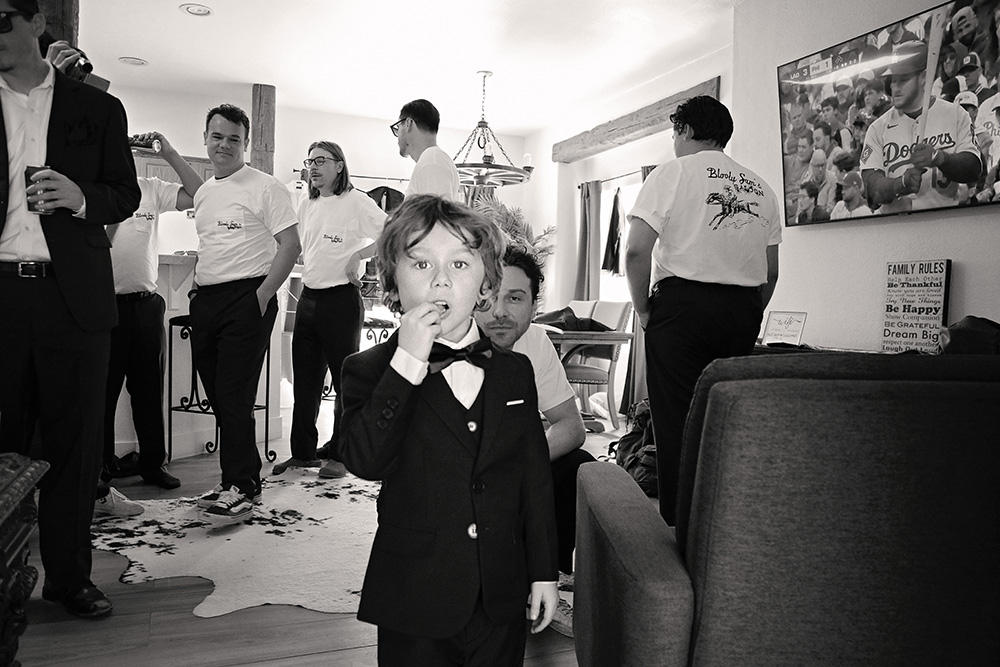 Young ring bearer in a suit standing among groomsmen during wedding preparations at Bubbling Wells Ranch, captured in black and white documentary wedding photography