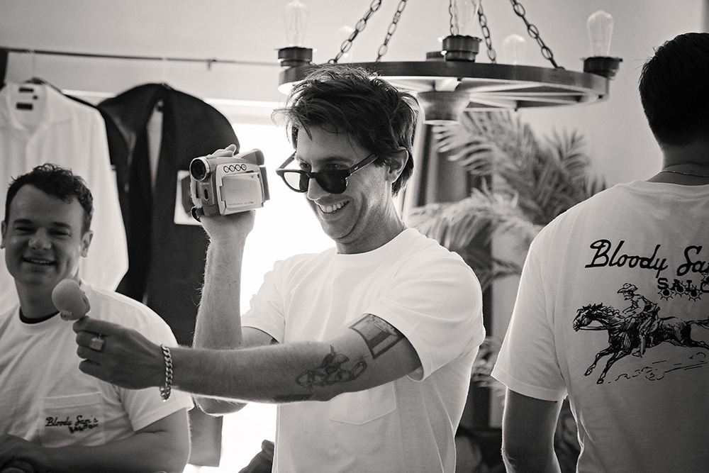 Groomsman filming with a handheld camcorder during wedding preparations at Bubbling Wells Ranch, captured in black and white documentary wedding photography