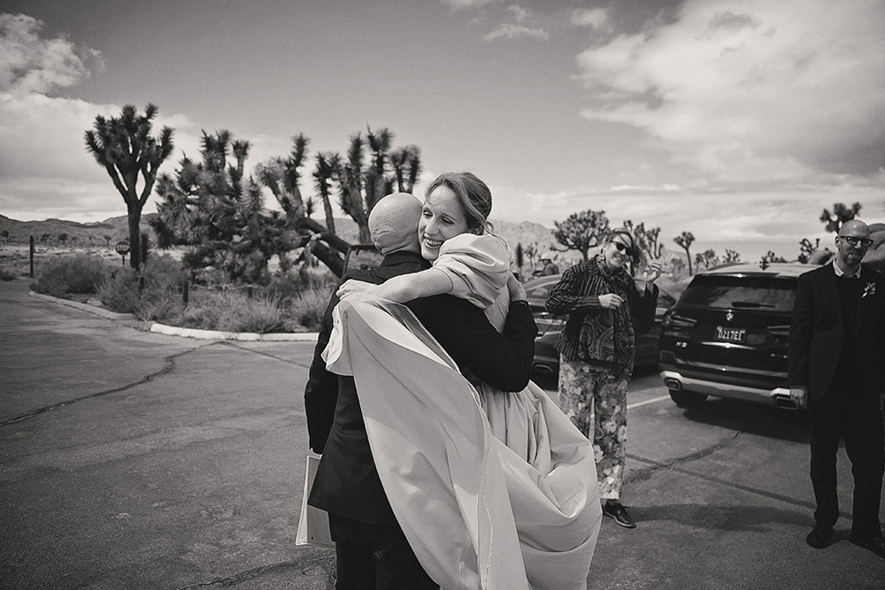 Bride embracing a guest during a small, intimate wedding at Joshua Tree National Park on a stormy afternoon, captured in black and white documentary wedding photography