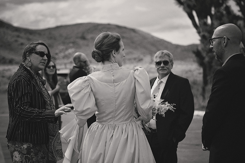 Bride greeting guests before an intimate wedding ceremony at Joshua Tree National Park on a cool, overcast day, captured in black and white documentary wedding photography