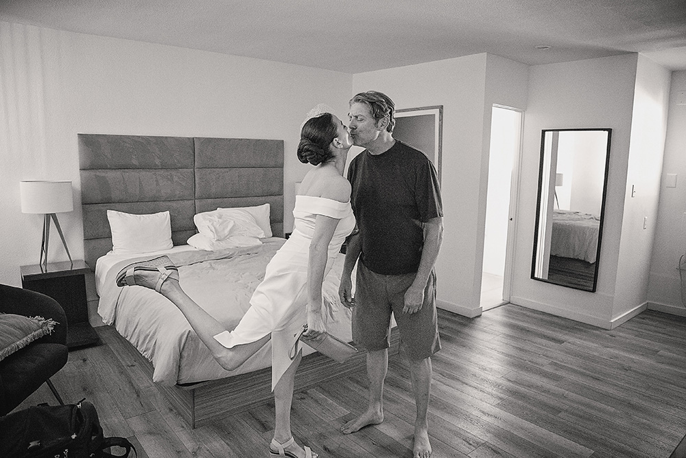 Bride and groom sharing a candid kiss inside their room at Skylark Hotel, captured in black and white documentary wedding photography