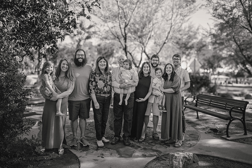 Three-generation family standing together outdoors in Palm Springs, smiling in soft sunlight, with grandparents centered and adult children and grandchildren gathered around.