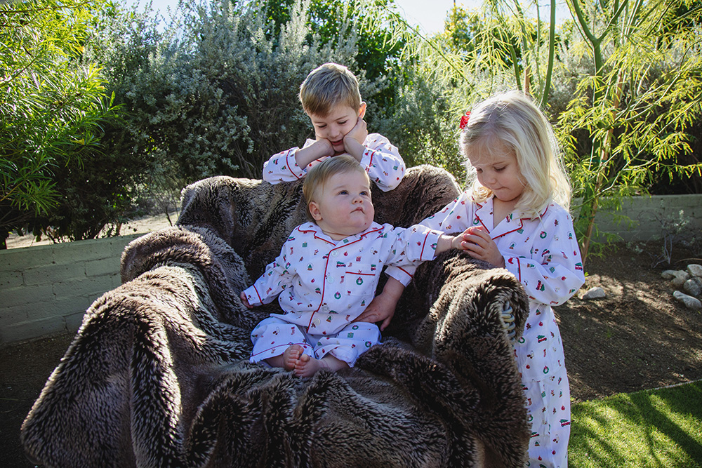 Three young siblings sitting together outdoors in pajamas during a candid Palm Springs family photography session.