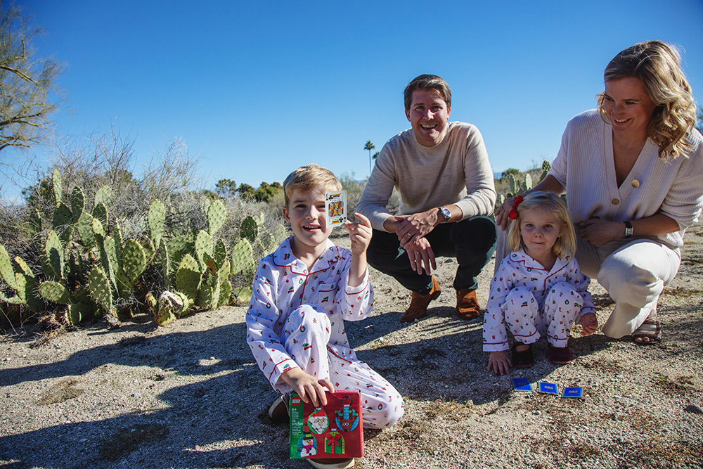 Family crouching together in the desert while children play with cards during a candid Palm Springs family photography session.
