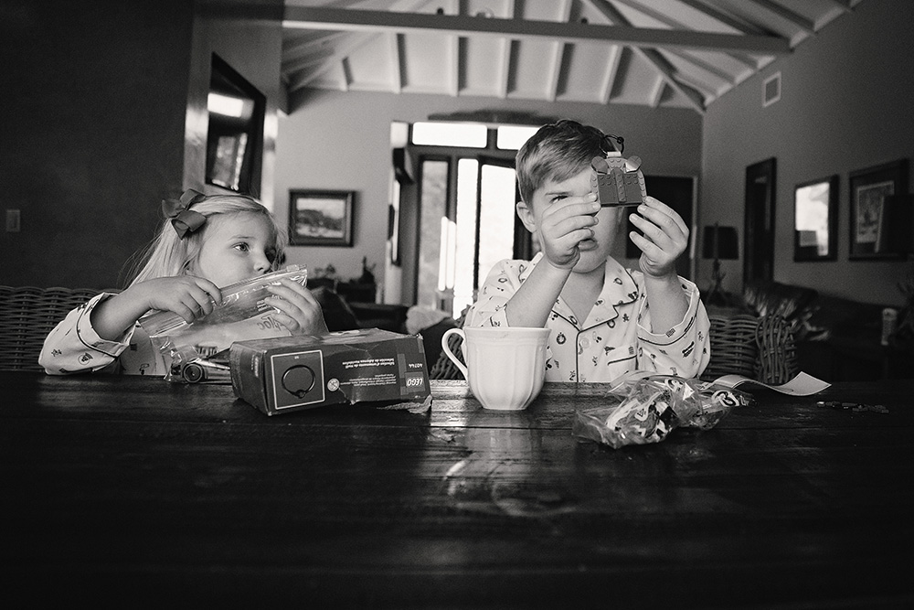 Black and white image of siblings sitting at a table, focused on small toys during a candid Palm Springs family photography session.