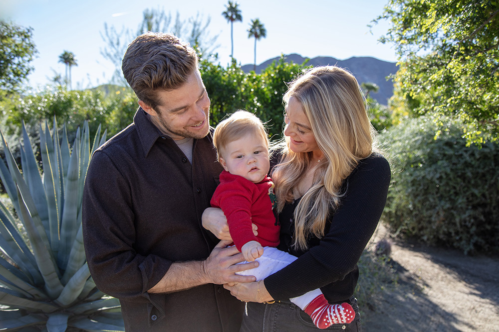 Palm Springs family portrait of parents holding their baby during a natural outdoor session surrounded by desert plants and palm trees in California