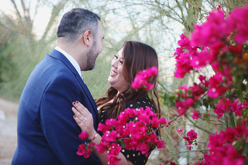 Beautiful image of a newly engaged couple sharing a sweet moment on the grounds of a hotel.  Vibrant bougainvillea in the forground