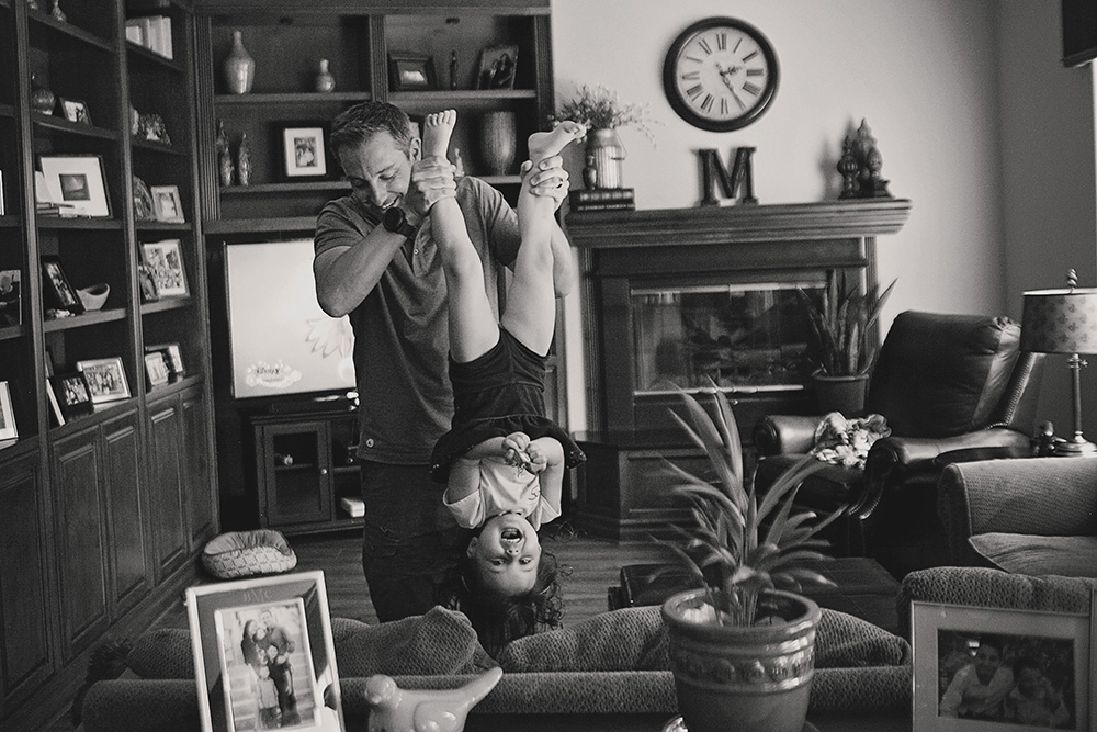 Father playfully holding his daughter upside down in the living room during a documentary day in the life family photo session.