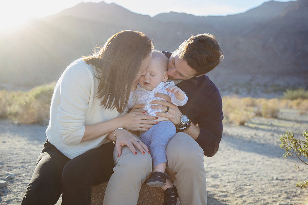 Family cuddling with their baby during a La Quinta Cove family photo session, sitting together in the desert with mountain views at golden hour.