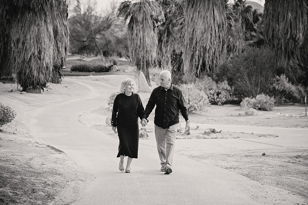 Black and white photo of an older couple walking towards the camera while chatting and laughing