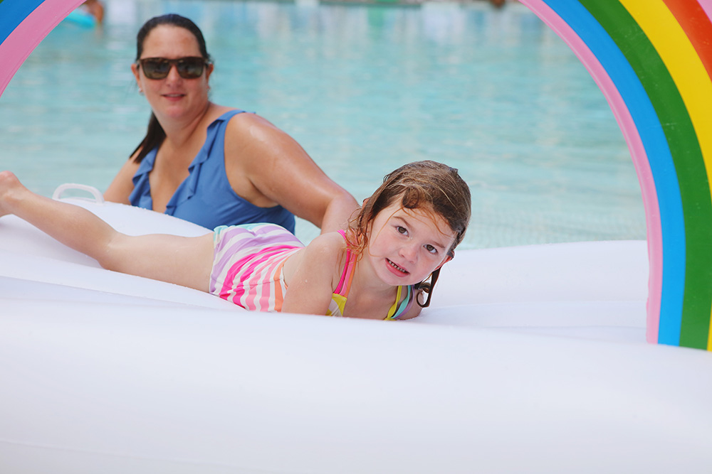 young girl floats around the pool on a rainbow floaty