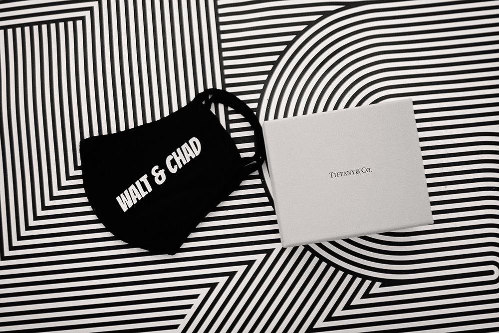 Black and white detail photo of custom “Walt & Chad” face masks beside a Tiffany & Co. ring box on a bold geometric patterned floor at the Avalon Hotel in Palm Springs during an intimate COVID-era wedding.