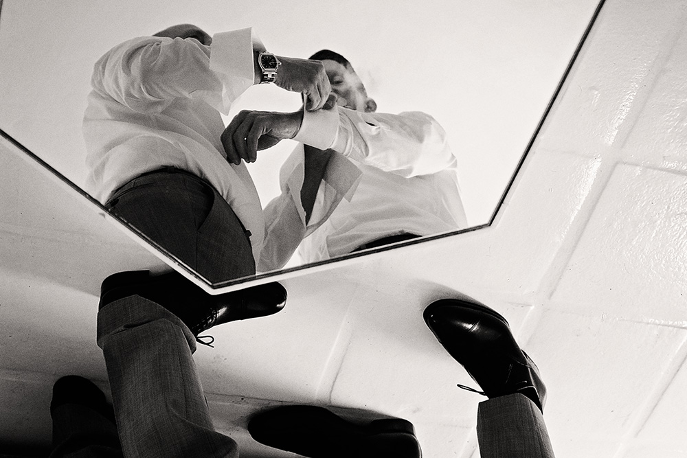 Black and white photo of a groom adjusting his cufflinks while standing over a mirror during wedding preparations at the Avalon Hotel in Palm Springs.